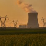Koeltoren van een kerncentrale met hoogspanningsmasten bij zonsondergang