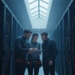 Drie engineers bekijken een tablet tussen serverracks in een datacenter