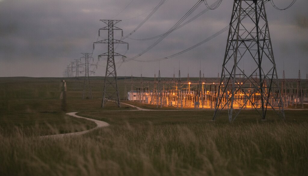 Hoogspanningsmasten en transformatoren van een onderstation in open landschap bij schemering